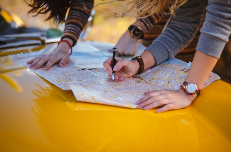 Women on summer road trip reading map for directions