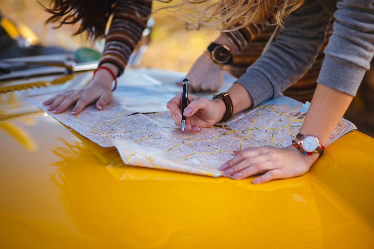 Women on summer road trip reading map for directions