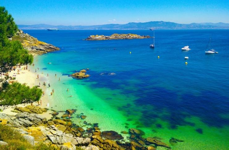 Beach with transparent green water in Cies Islands, in Galicia, Spain, with boats docked in front of