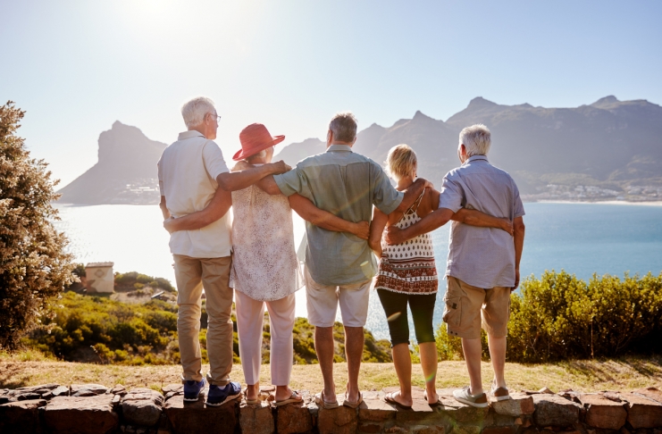 Rear View Of Senior Friends Visiting Tourist Landmark On Group Vacation Standing On Wall